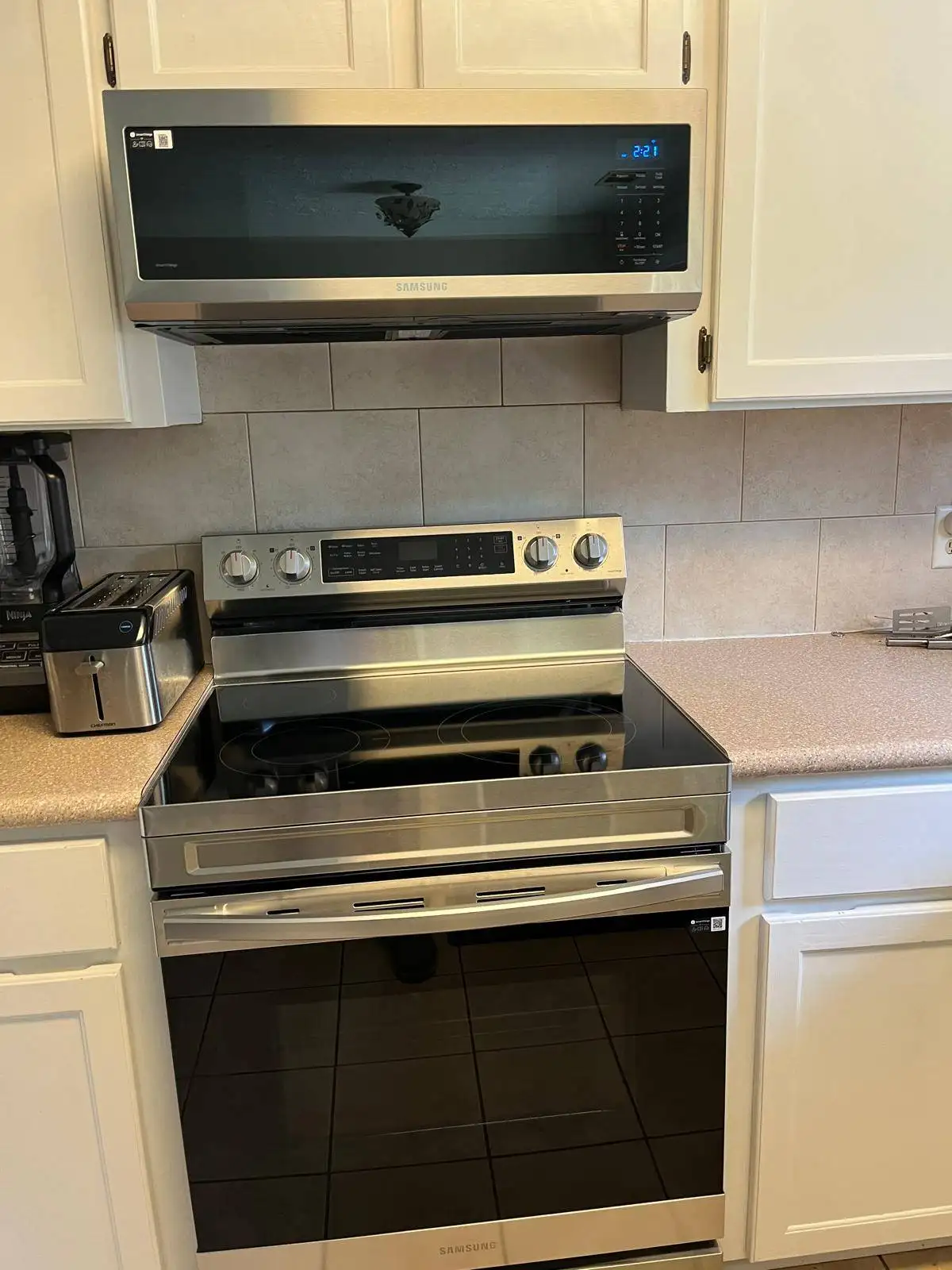 Stainless steel Samsung over-the-range microwave and electric range with a glass cooktop in a kitchen with white cabinets