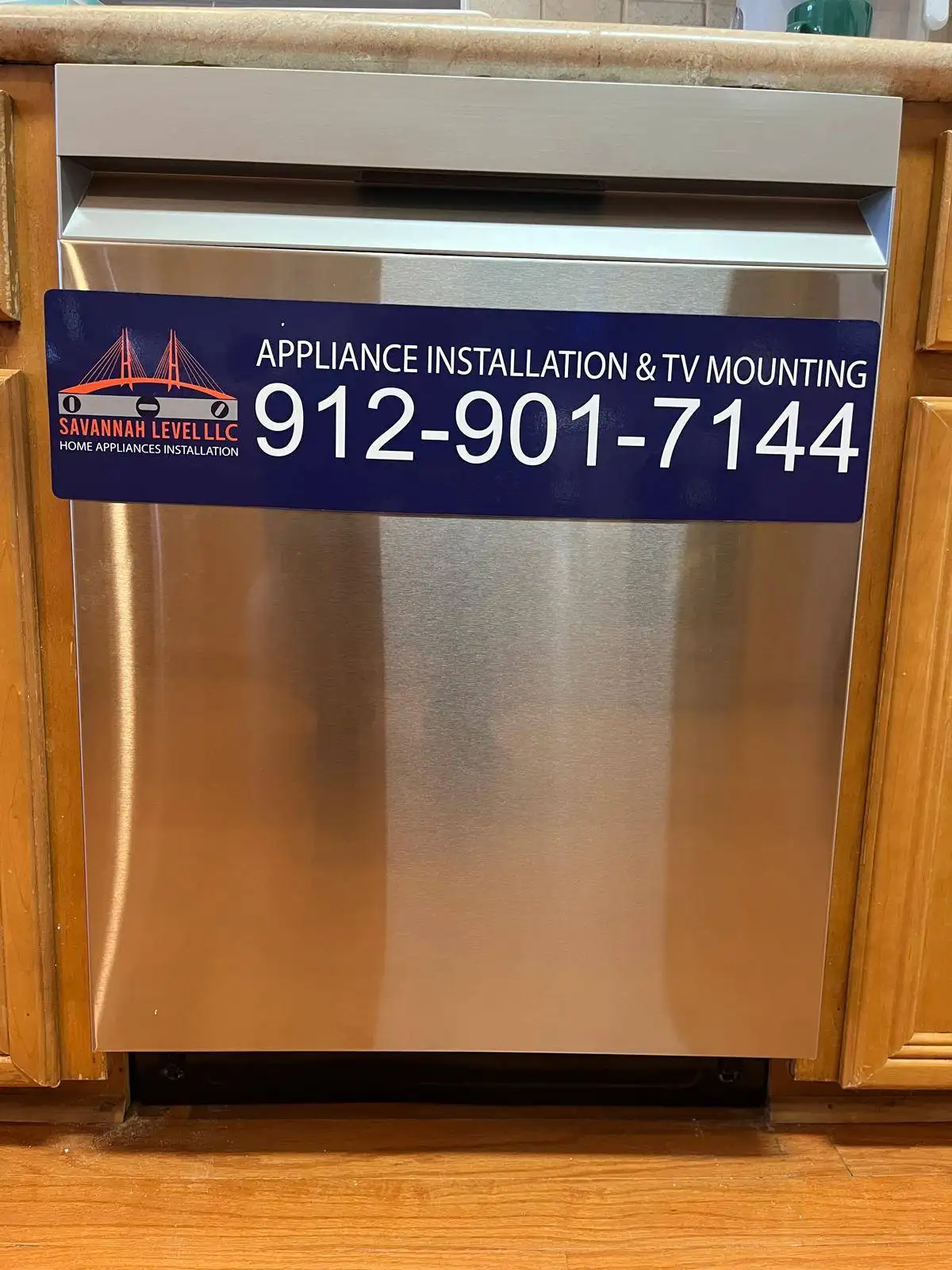 Stainless steel built-in dishwasher with a Savannah Level LLC appliance installation and TV mounting magnet, between wooden kitchen cabinets